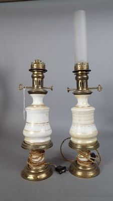 une paire de lampes blanches et dorées posées sur une étagère, avec un tableau accroché au mur en arrière-plan