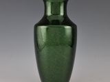 un vase vert posé sur une table blanche, près d'un mur gris