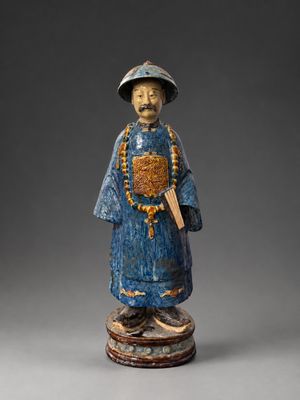 une vieille statue en bois représentant un homme coiffé d'un chapeau et muni d'une canne