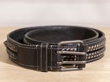 ceinture en cuir noir avec des boucles argentées posée sur une surface en bois