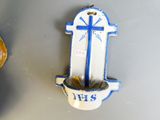 une croix bleue et blanche accrochée au mur à côté d'une plante en pot