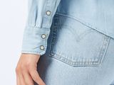 the back of a woman in a blue shirt and jeans with her hands in her pockets