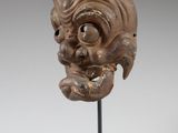 a wooden mask on a black stand with a white background