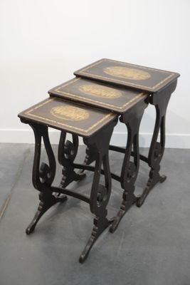 trois tables gigognes anciennes, noires et dorées, posées sur un sol gris