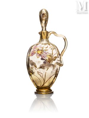 une image représentant un vase en verre muni d'une anse dorée, posé sur une surface blanche