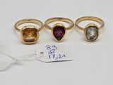 three rings with different colored stones and a price tag on a white surface
