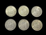 six silver coins of different sizes and shapes on a black background