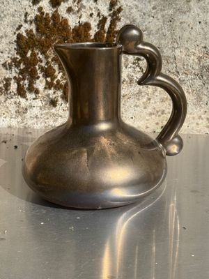 un vase en argent posé sur une table, avec un mur en pierre en arrière-plan