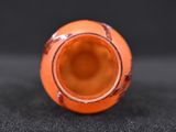 a small orange vase sitting on a black surface