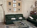 un salon avec un canapé, un fauteuil, une table basse et des tableaux accrochés au mur