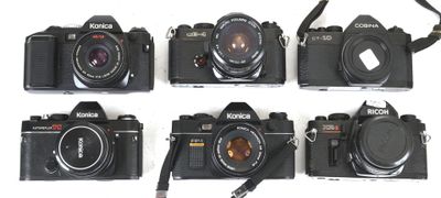six cameras are lined up on a white surface with a camera strap