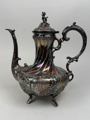 silver plated tea pot with ornate design on stand