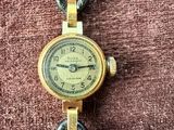 une photo d'une montre-bracelet en or posée sur un tissu marron