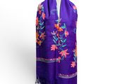 une écharpe violette ornée de fleurs colorées et de franges, posée sur un mannequin