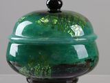 a green glass container with a black lid on a table
