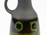 a green and black vase with a face on it