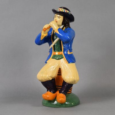 figurine représentant un homme vêtu d'un manteau bleu et d'un chapeau, jouant de la flûte