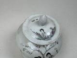 a white jar with a painting on it on a table