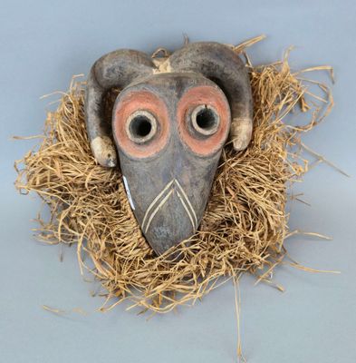 un masque d'oiseau en argile posé sur un lit de paille