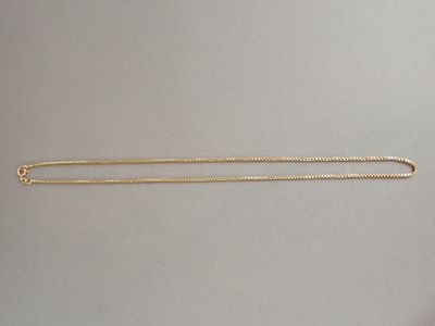 un collier en or avec une longue chaîne posée sur une surface grise