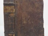an old brown book sitting on top of a table next to a white wall
