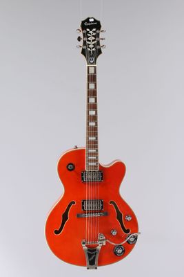 an orange electric guitar hanging from a string on a white wall