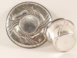 a silver cup and saucer sitting on a white surface