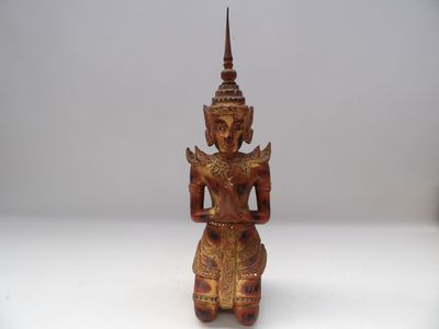 une vieille statue en bois représentant une personne assise sur une surface blanche