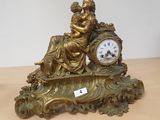 a gold clock sitting on a table with a woman holding a baby