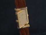 une image d'une montre en or avec un bracelet en cuir marron