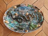 une assiette en céramique ornée d'un serpent, posée sur un plancher en bois
