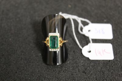une image représentant une bague ornée d'une pierre verte posée sur une surface noire