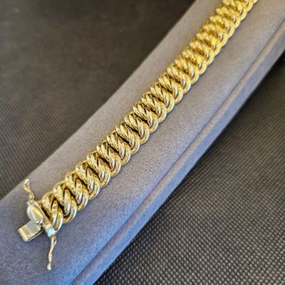 gros plan d'un bracelet en chaîne en or sur une surface noire