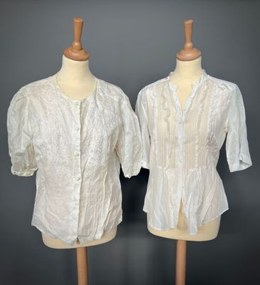 two mannequins with white blouses on display against a gray background