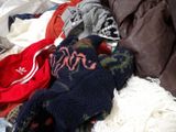 a pile of sweaters and mittens on a bed