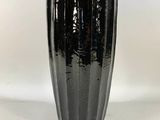 tall black vase with a white flower in it on a white background