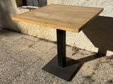a wooden table with a black metal base on the sidewalk