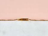 un bracelet en or avec une barre suspendue à une chaîne, sur fond rose