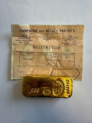 un vieux lingot d'or posé sur une feuille de papier, à côté d'un ticket de caisse