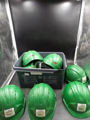 Plusieurs casques de chantier verts sont posés dans un bac posé à même le sol.