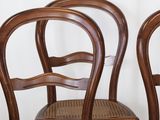 three wooden chairs with wicker seats sit in front of a white wall