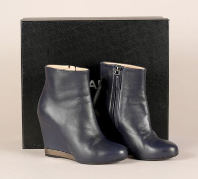 une paire de bottines à talons compensés en cuir bleu, dans une boîte noire