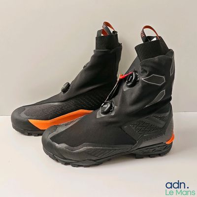 une paire de chaussures de ski noires et orange posées sur une surface blanche
