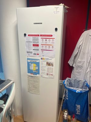 a white refrigerator in the corner of a room with clothes hanging on the wall
