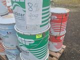 Plusieurs seaux de peinture sont empilés sur une palette dans un parking
