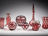 Plusieurs vases en verre rouge sont alignés sur une surface blanche