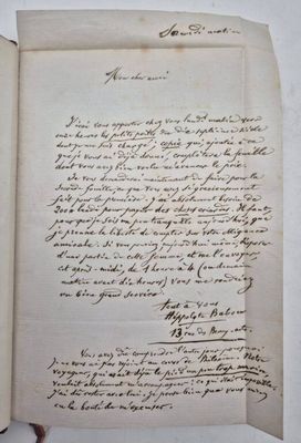 un livre ouvert, sur lequel repose une lettre manuscrite, posé sur une table