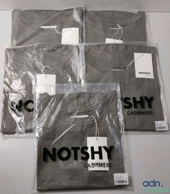 trois t-shirts sont emballés dans des sacs en plastique sur une table
