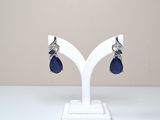 une paire de boucles d'oreilles en verre bleu et argent, posée sur un socle blanc