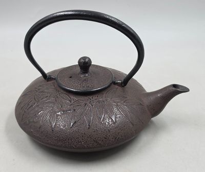 une théière marron avec une anse, posée sur une table blanche